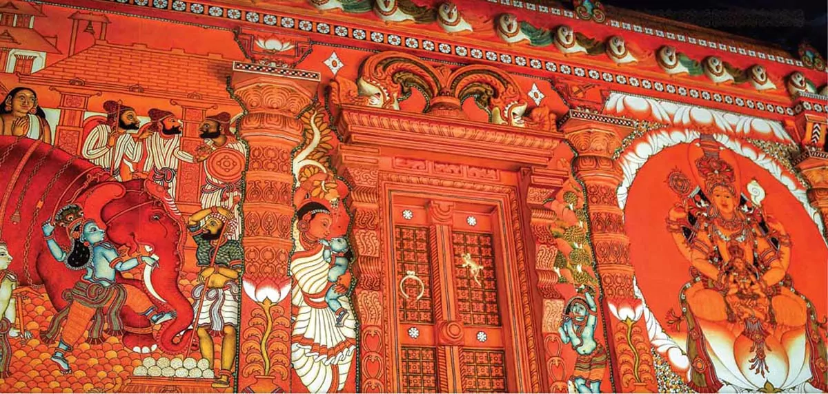 A red temple wall features Kerala Mural Painting with religious murals adorning nooks and crevices.